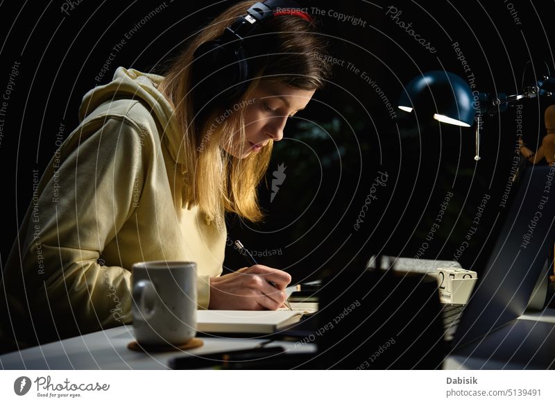 Frau, die nachts mit Kopfhörern Musik hört und einen Laptop benutzt heimwärts Nacht Bildung arbeiten Hausaufgabe benutzend lässig Kaffee Hochschule Mitteilung