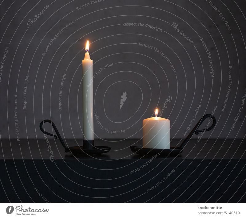 Zwei Kerzen in schwarzen Kerzenständern mit Haltegriff brennen vor einer Betonwand. Kerzenschein dünn dick Wachs Trauer Vergänglichkeit Hoffnung