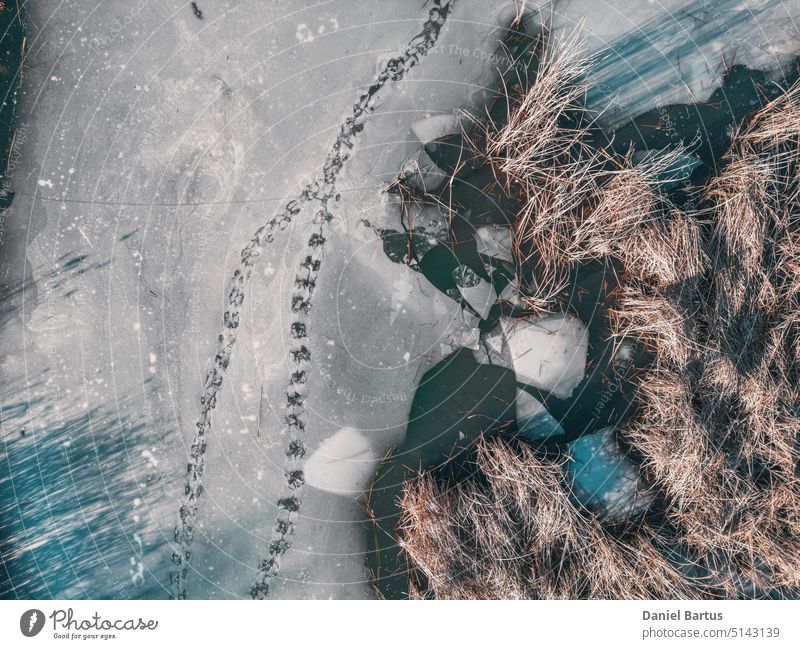 Panoramablick auf einen zugefrorenen See mit Tierspuren und rissigem Eis. Tierspuren auf der gefrorenen Oberfläche des Sees. Gesprungenes Eis auf dem See