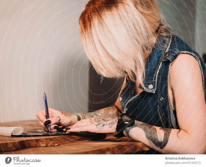 Tattoo-Künstlerin Zeichnung Illustration des Schädels in Tinte Studio. Frau mit schwarzen Nägeln und Ringen bei der Arbeit. Neue Mode Lebensstil künstlerische Trends Konzept. Warm kinematischen Filter.