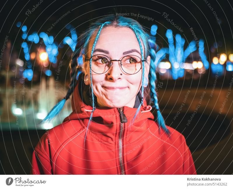 Junge schöne Mädchen mit blau gefärbten ungewöhnliche Haare, transparente Brille, Piercing stehen in der Nacht Straße mit Neonröhren Hintergrund. Porträt des glücklichen niedlichen stilvollen Teenager.