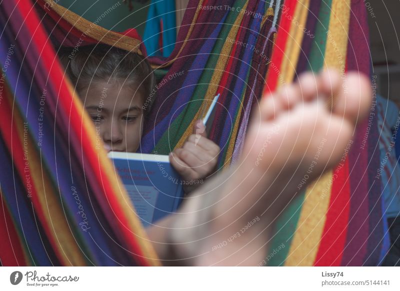 Lesendes Mädchen, tief in ein Buch vertieft, streckt ihre Füße aus einer bunt gestreiften Hängematte Kind Kindheit Kinderzimmer bunt gemischt lesen Fuß Barfuß