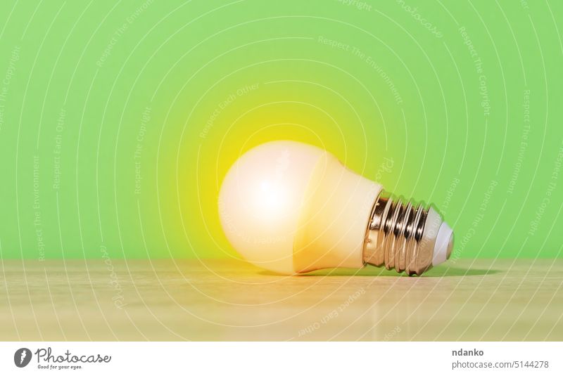 Eine weiße Glaslampe leuchtet mit gelbem Licht auf grünem Hintergrund. Neue Idee Knolle Energie Innovation Technik & Technologie Konzept Elektrizität Erfindung
