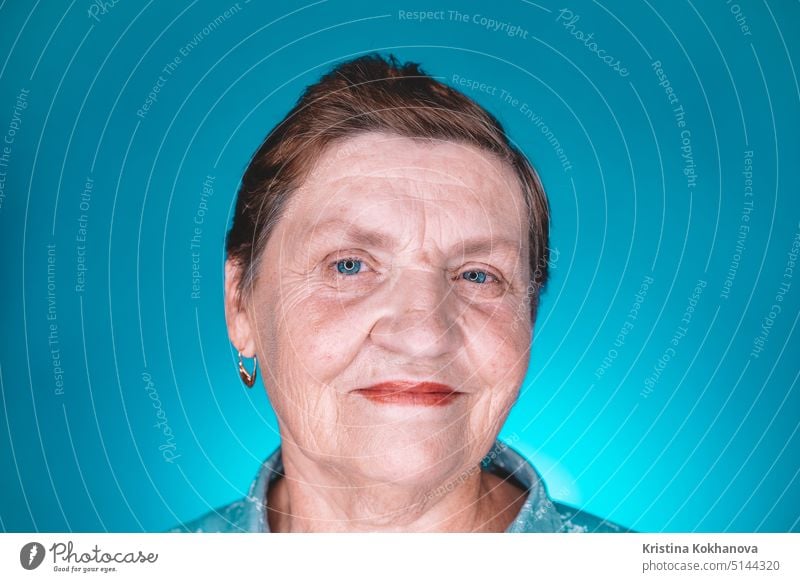 Kaukasische freundliche Großmutter schaut in die Kamera. Porträt der lächelnden alten Frau im Studio auf blauem Hintergrund. Lebensalter Holunderbusch älter gut