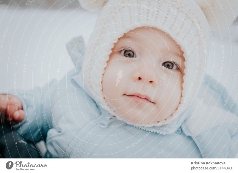 Nettes Porträt von kleinen Baby in Wintermütze mit flauschigen Ohren auf verschneiten Straße Hintergrund. Familie, Sohn, Kleinkind Kind Konzept. Kindheit