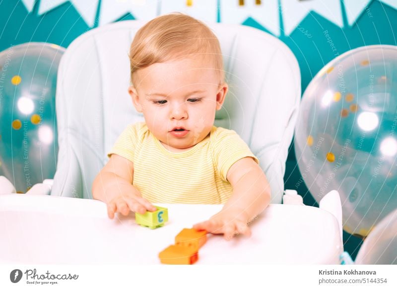 Cute Baby Junge sitzt in seinem Stuhl und spielen mit bunten Ziegeln. Geburtstag hübsches Kleinkind Kind mit großen Augen Porträt. Lustiges Kind. Spielen