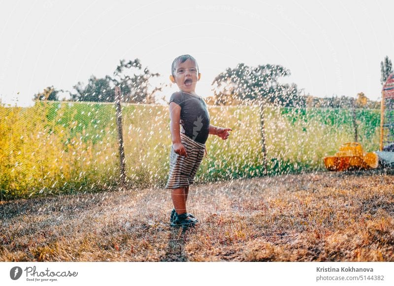 Glücklich adorable Kleinkind Junge Spaß unter regen haben. Baby lacht, er ist sehr froh, Wetter. Person Kind Regen im Freien Spielen Tropfen Kindheit Herbst Tag
