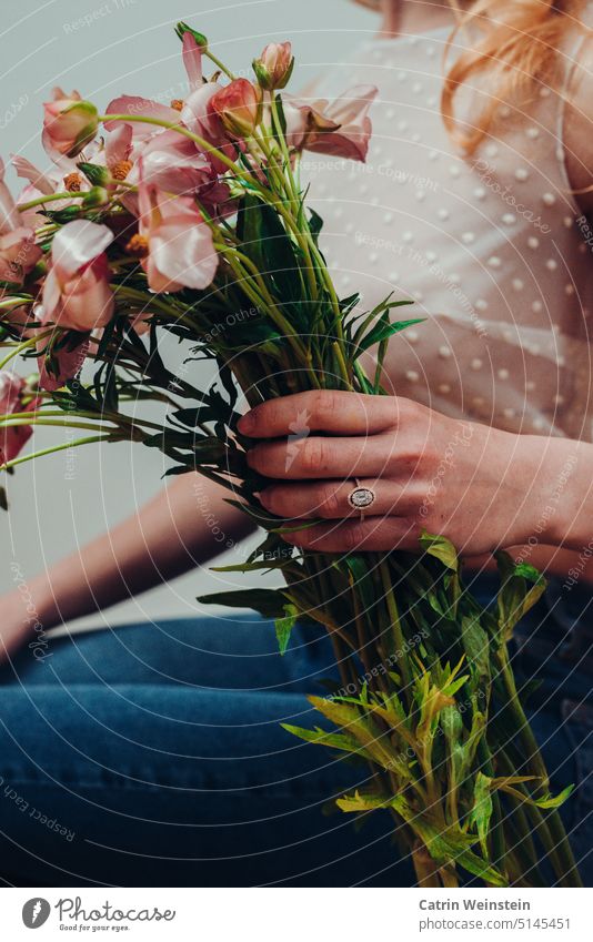 Frau mit Ring am Finger hält Blumen in der Hand Diamant gold Schmuck Blumenstrauß Top Jeanshose Punkte grün rosa rosa Blumen