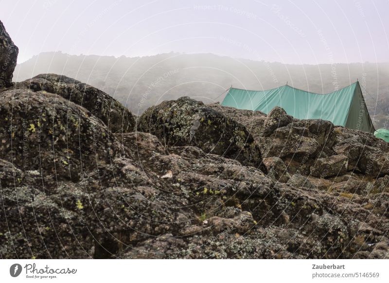 Grünes Zelt der Träger hinter Felsbrocken in Wolken und Nebel am Kilimanjaro, Shira Camp 2 bunt Felsen Wandern Trekking Bergsteigen Abenteuer anstrengend