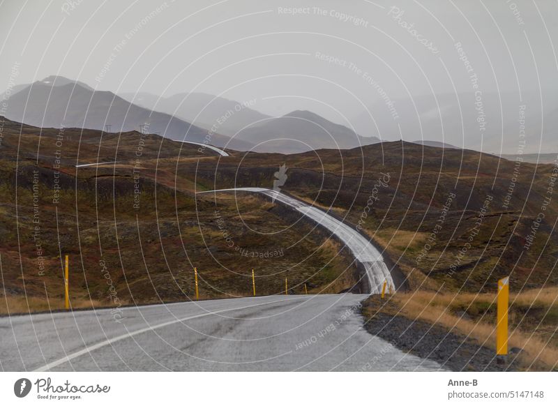Straße die in einer weichen Zickzackkurve über bemooste Hügel führt , an einem regnerischen Tag fotografiert . Der Hintergrund verschwindet im Dunst.  Nordisland.