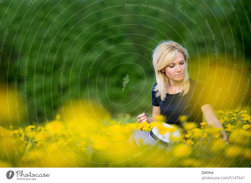 Eine junge blonde Frau ruht sich auf einer blühenden Löwenzahnwiese aus, ein Porträt in Frühlingsstimmung schöne Frau Löwenzahnfeld Blüte Blühend Überstrahlung