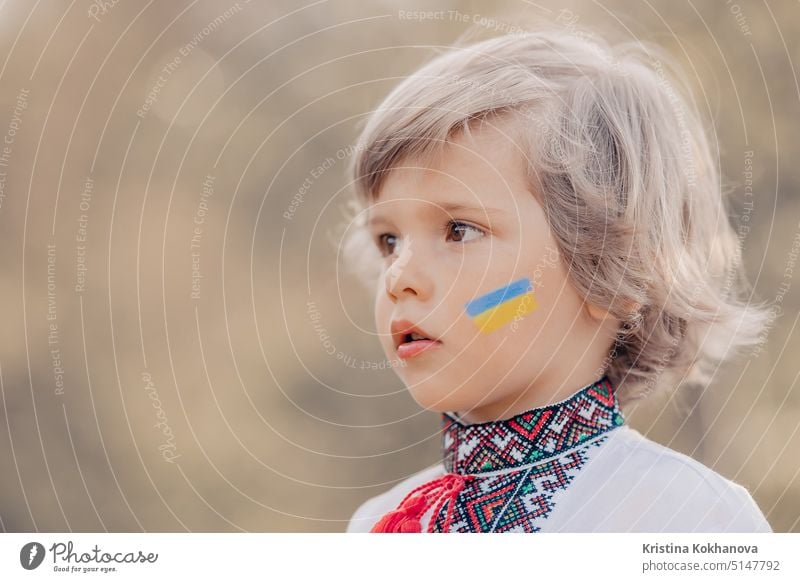 Porträt des kleinen ukrainischen Jungen mit blauer gelber Flagge Kunst auf der Wange. Kind in traditioneller Stickerei vyshyvanka Shirt. Ukraine, Freiheit, Nationaltracht, Sieg im Krieg. Kopieren Raum
