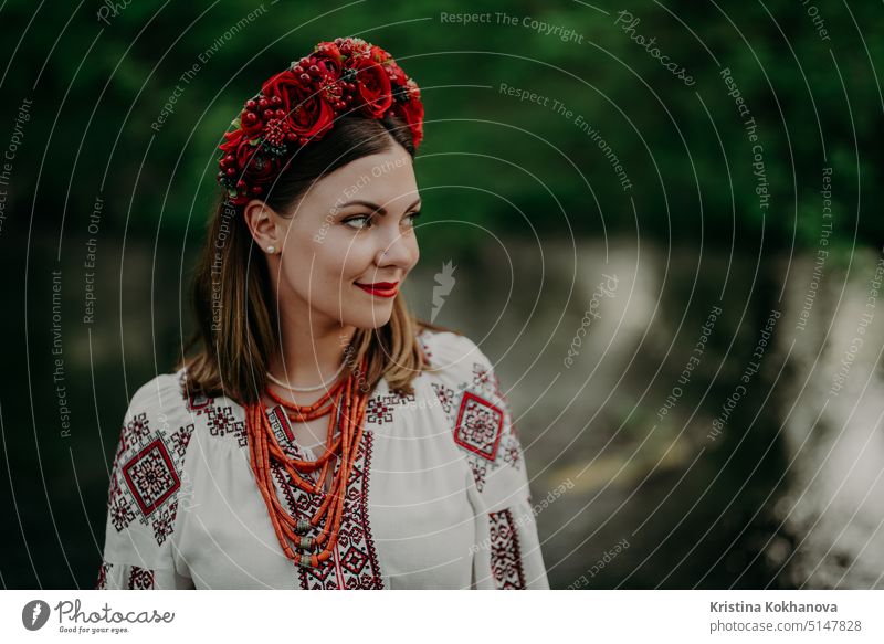 Hübsche ukrainische Frau in traditioneller Stickerei vyshyvanka Kleid und rote Blumen Kranz in der Nähe von Fluss. Ukraine Freiheit, Frühling, Nationaltracht, Sieg im Krieg.