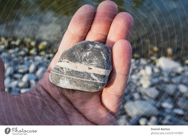 Grauer Stein mit weißen Streifen in einer Hand mit einem Fluss im Hintergrund Ackerbau Asien Rassen Gebäude Zement Chlorid Kristalle Extraktion Bauernhof Finger