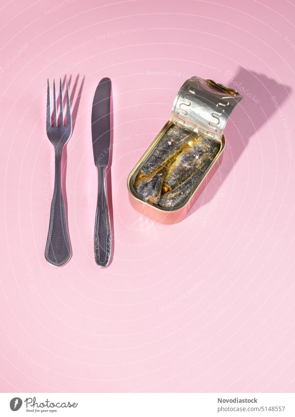 Sardinen in einer Dose, ein Messer und eine Gabel, bereit zum Verzehr, kein Teller, isoliert auf rosa Hintergrund Büchse Konservendose Dosennahrung