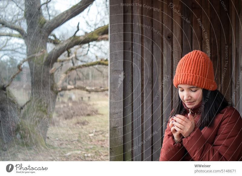 Eine junge Frau ruht sich auf einer winterlichen Wanderung aus und wärmt sich die Hände an einem warmen Teebecher Kälte Wärme Winter draußen Natur wandern