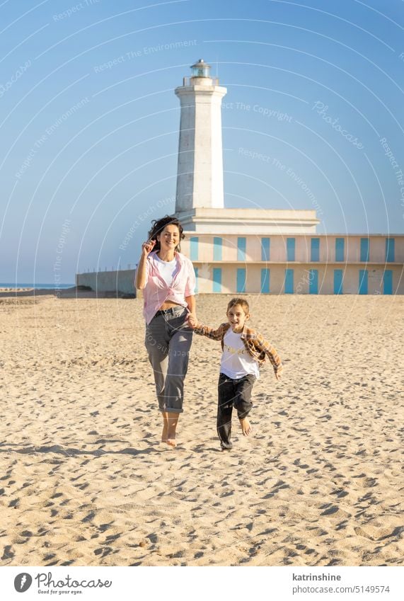 Glückliche Mutter und Sohn laufen am Strand barfuß in einem sonnigen Tag gegen den Leuchtturm Barfuß MEER Sonnenuntergang im Freien Kleinkind kleiner Junge Kind