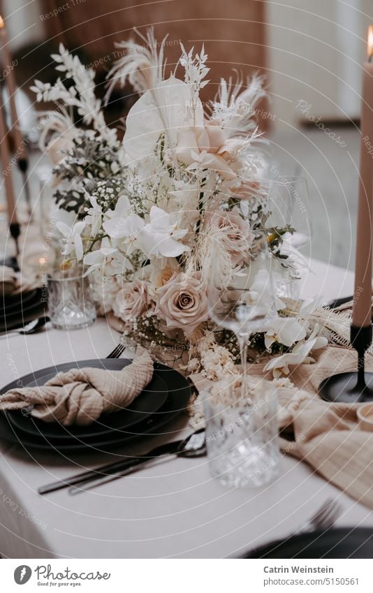 Tischdekoration in Altrosa und weiß. Centerpiece mit Rosen, Blumen und Federn. Außerdem stehen Kerzen, schwarze Teller, Gläser und Besteck auf dem Tisch.