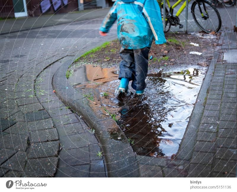 Kind in Matschklamotten patscht in eine Pfütze Kindheit Wasser matschen patschen Regenklamotten Freude nass dreckig Gummistiefel Stadt Spielen Matschkleidung