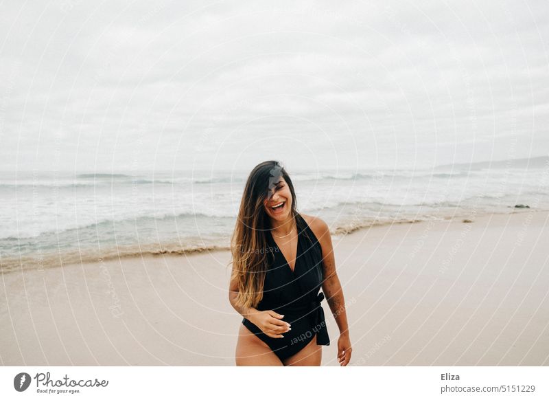 Lachende junge Frau mit Haaren im Gesicht im Badeanzug am Strand Meer lachend Freude Gute Laune positiv Urlaub Lebensfreude Lächeln Zufriedenheit Fröhlichkeit