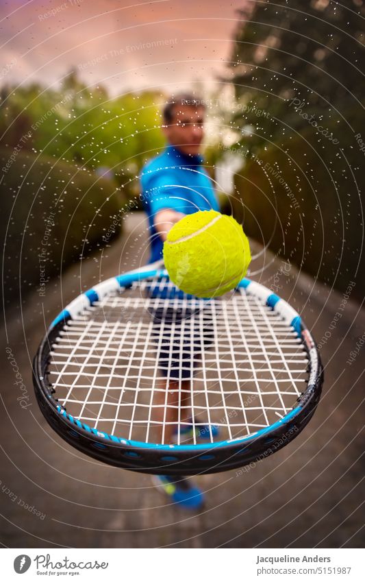 Mann hält einen Tennisschläger mit rotierendem und Wasser spritzendem Ball in Richtung Kamera - ein lizenzfreies Foto von Photocase