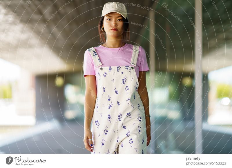 Stilvolle asiatische Frau geht auf die Kamera zu Vorschein Spaziergang modern Gebäude Straße urban Outfit Porträt jung ethnisch T-Shirt gesamt Verschlussdeckel