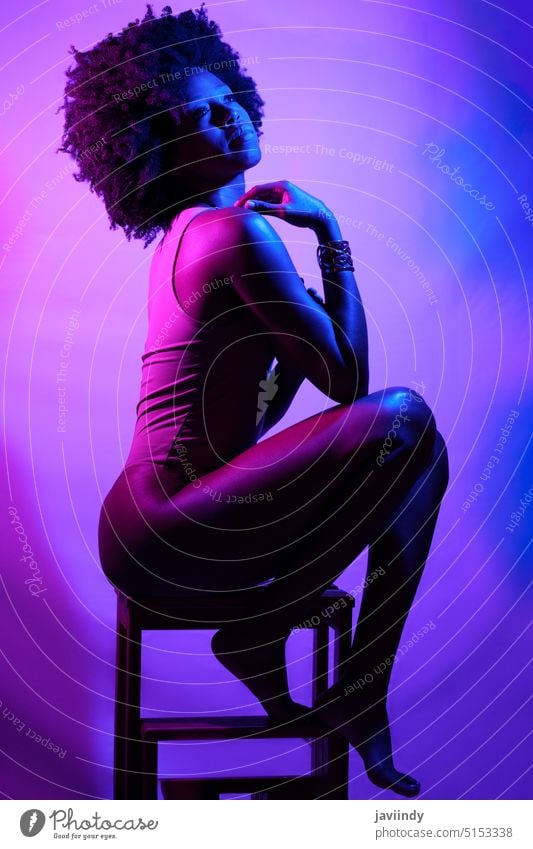 Sinnliche schwarze Frau unter Neonlicht Schulter berühren sinnlich neonfarbig violettes Licht Hocker Model schlank Body leuchten Afroamerikaner ethnisch lebhaft