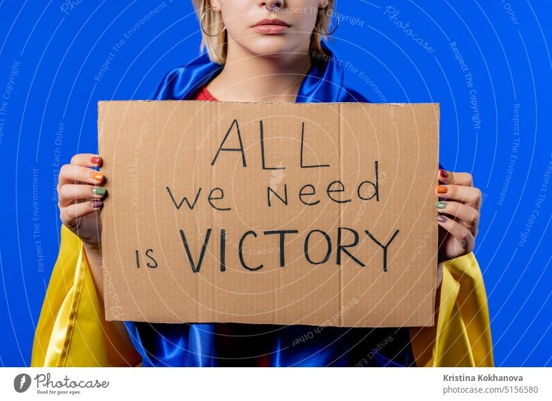 Ukrainische Frau mit Karton All we need is victory auf blauem Hintergrund. Ukraine protestieren Ukrainer Kundgebung Fahne Politik Freiheit politisch stoppen