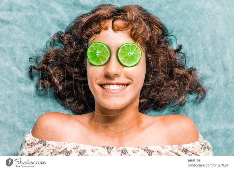 Junges Mädchen mit lächelnden Augen, die mit Limettenscheiben bedeckt sind Kalk Zitrone grün krause Haare Schulter Lächeln Teenager Zähne Bräune