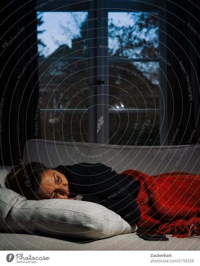 Eine Frau ruht auf dem Sofa mit roter Decke, draußen ist es kalt ausruhen Ruhe schlafen wärmen Warm Kälte Winter friedlich entspannt Entspannung Erholung liegen