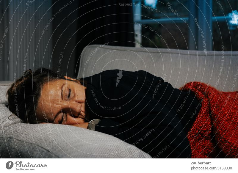 Eine Frau ruht auf dem Sofa mit roter Decke und im schwarzen Pullover, draußen ist es kalt ausruhen Ruhe schlafen wärmen Warm Kälte Winter friedlich entspannt