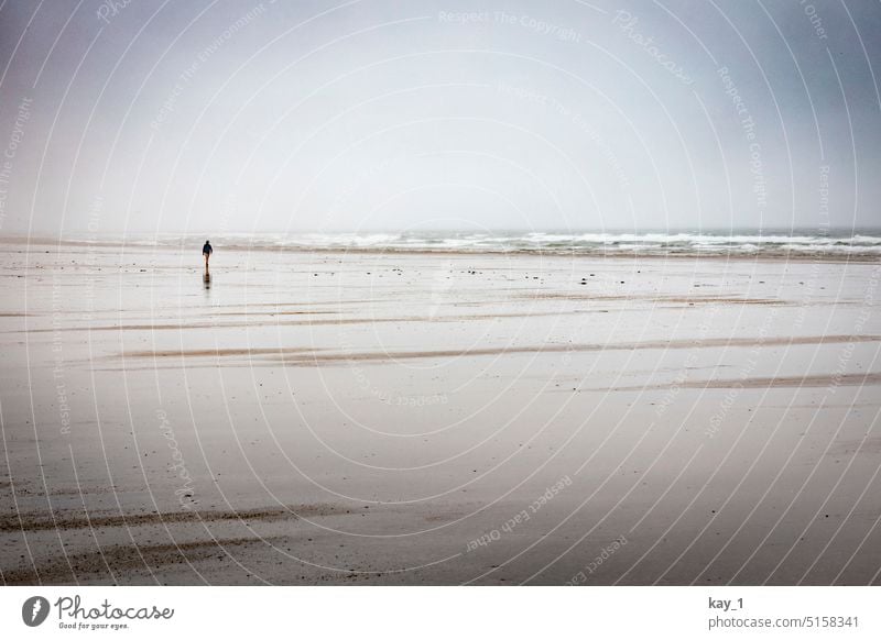 Strand mit Person in der Ferne bei stürmischem Wetter Sand Wattenmeer Nordsee Atlantik Atlantikküste Strandspaziergang Mensch Einsamkeit dunkle Wolken Meer