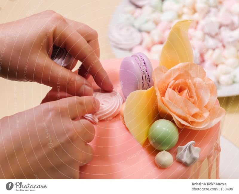 Unerkennbare Frau dekoriert Mousse-Glasur-Torte mit Rose, Macarons, Hände Detail, Fokus auf den Kuchen. DIY, Sequenz, Schritt für Schritt, Teil einer Serie.