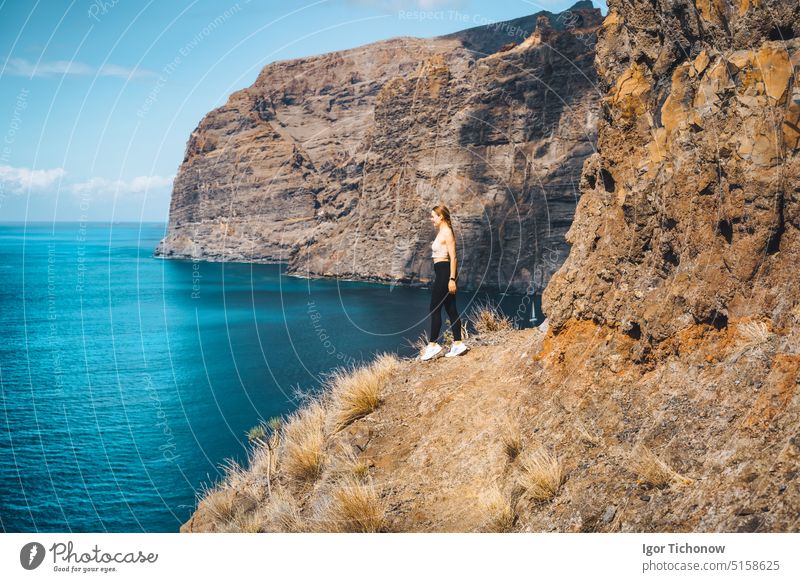 Unabhängige entspannt ruhig schlankes Mädchen Tourist steht auf dem Rand einer Klippe mit erstaunlichen Meer und Himmel Blick. Los Gigantes Bergketten. Teneriffa. Santiago del Teide. Kanarische Inseln, Spanien.