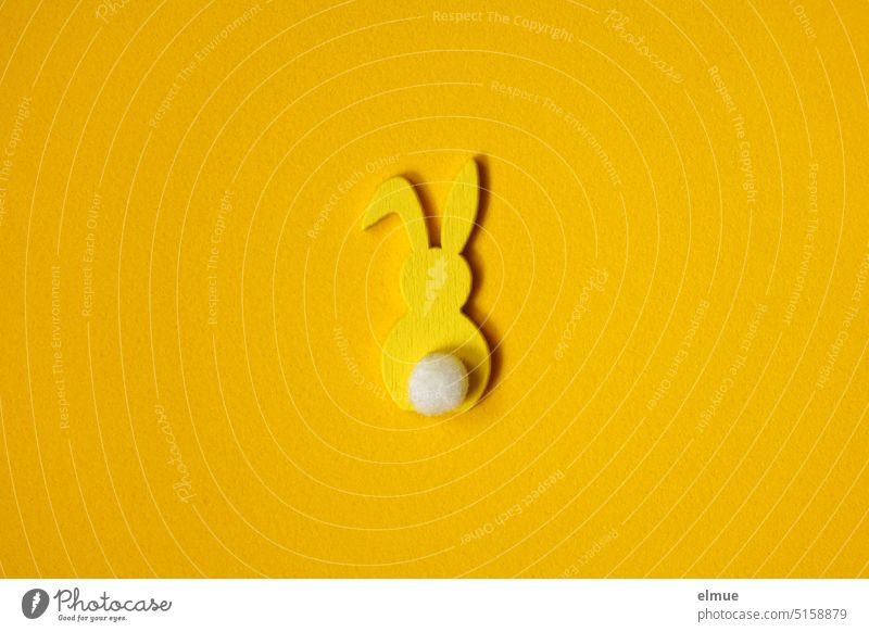 gelber, stilisierter Osterhase von hinten mit Knickohr und weißer Blume auf gelbem Untergrund / Ostern Hase & Kaninchen Hasenohren Deko Osterdekoration