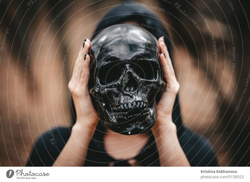Eine Hexe in schwarzer Kleidung hält einen Schädel in Kopfhöhe. Todesser Konzept anatomisch Anatomie Hintergrund kahl biologisch Biologie Körper Knochen Gehirn