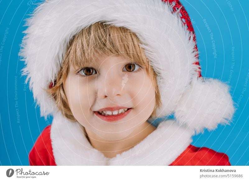 Porträt eines niedlichen Jungen mit Weihnachtsmannmütze auf blauem Studiohintergrund. Weihnachten 4 Jahre alt bezaubernd künstlicher Bart Baby