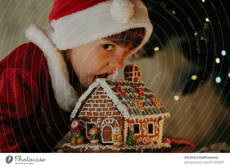 Niedlicher kleiner Junge im Weihnachtsmannkostüm isst Lebkuchenhaus, Weihnachten 4 Jahre alt bezaubernd künstlicher Bart Baby Baby-Weihnachtsmann feiern Feier