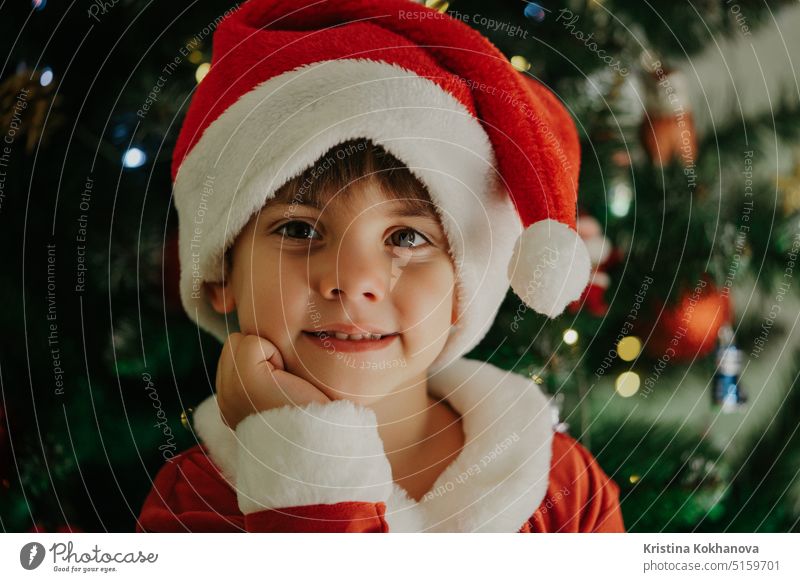 Porträt eines niedlichen Jungen im Weihnachtsmannkostüm auf einem Weihnachtsbaum-Hintergrund. 4 Jahre alt bezaubernd künstlicher Bart Baby Baby-Weihnachtsmann