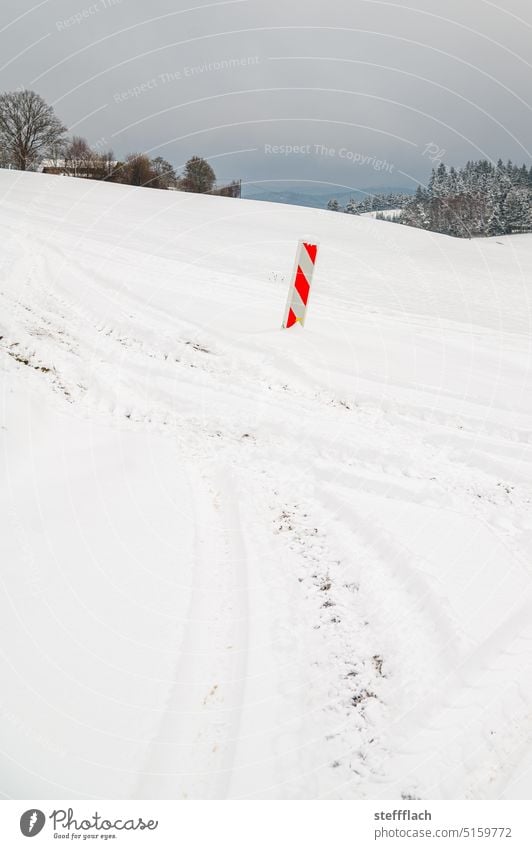 Rot-Weiße Warnbake einsam in weißer Schneelandschaft auf dem Feld Baustelle Winter Landschaft grau Wald Bäume Himmel Reifenspuren Eifel Stille Einsamkeit