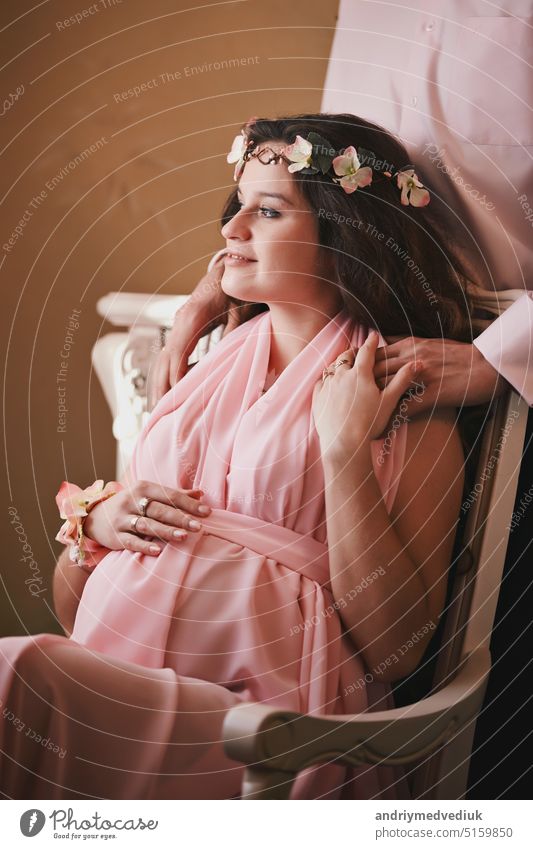 schwangere Frau in einem rosa Kleid auf einem Stuhl sitzend hinter einem lächelnden Mann stehend. ein Baby erwartend Zusammensein schön Lächeln Schwangerschaft