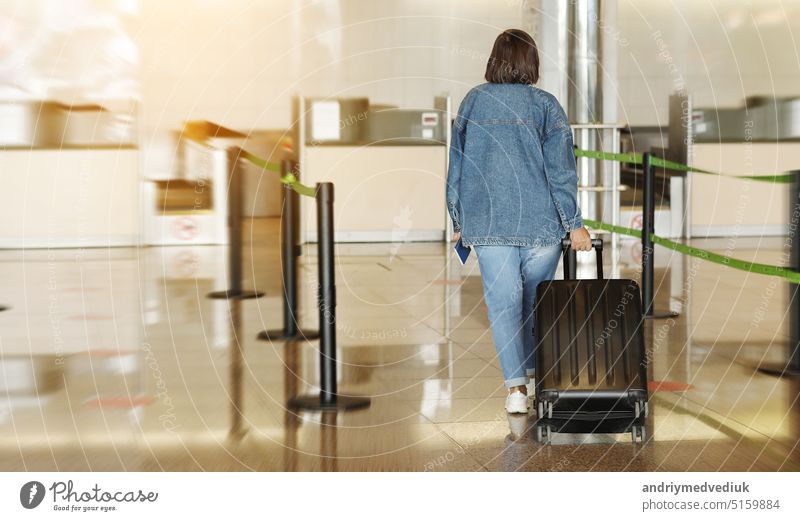 Rückenansicht einer Frau mittleren Alters, die in Freizeitkleidung reist. Frau im Flughafen mit Koffer geht am Check-in-Schalter beim Einchecken für ihren Flug. Passagier reisen im Ausland auf Urlaub oder Wochenende
