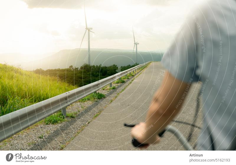 Selektiver Fokus auf einen Windpark mit der Rückansicht einer Person auf einem Fahrrad im Vordergrund. Windenergie. Windkraft. Nachhaltige, erneuerbare Energie. Windturbinen erzeugen Strom. Nachhaltiger Lebensstil.