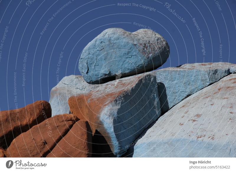 Von einem Künstler hellblau angemalte abgerundete Felsen. Ganz oben liegt ein schwerer rundlicher Brocken. Dahinter blauer Himmel. Kunst Natur himmelblau