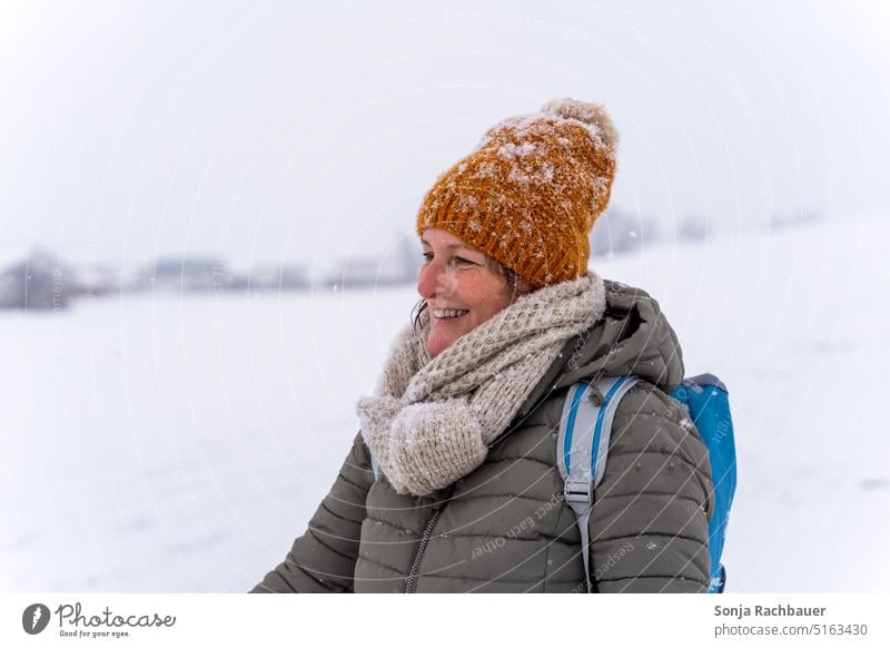 Eine lächelnde Frau mit Mütze und Schal im Schnee Lächeln Winter kalt Gesicht 50 plus feminin natürliche Schönheit Porträt 1 Außenaufnahme wandern glücklich