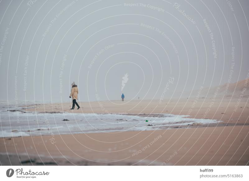 zwei Menschen am weiten Strand mit Sandsturm, Nebel und diesiger Sicht. Brandung Dänemark Sandstrand Herbst Strandspaziergang Sturm Verwehung Weite Winter