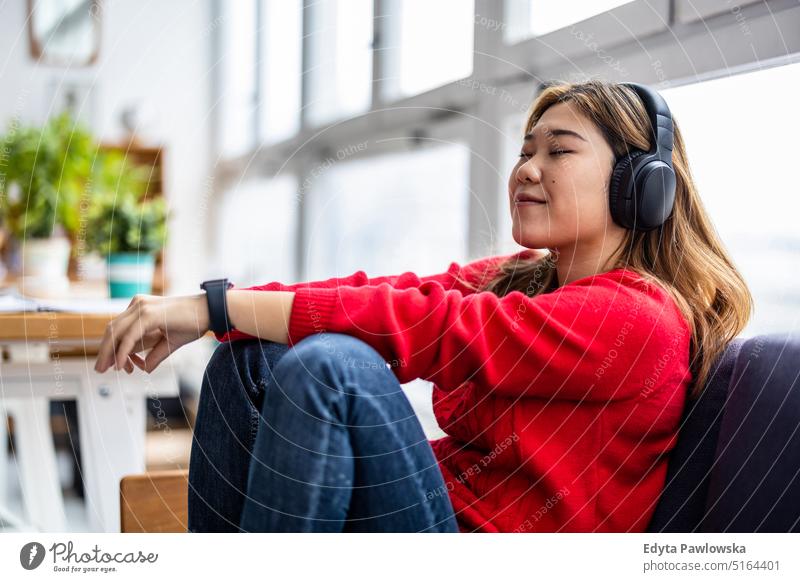 Junge Frau mit Kopfhörern beim Entspannen auf dem Sofa echte Menschen Jahrtausende Schüler im Innenbereich Loft Fenster natürlich Mädchen Erwachsener eine