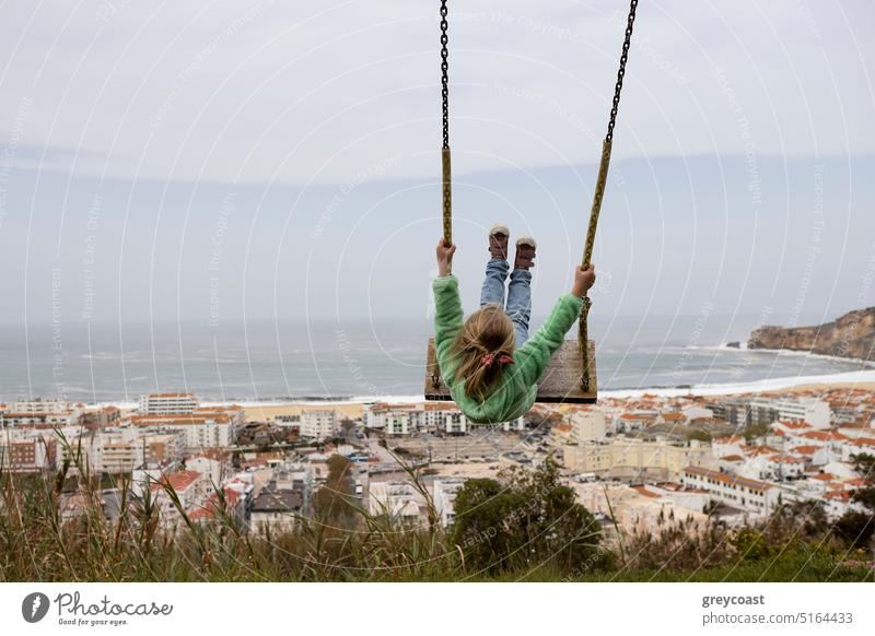 Kleines Mädchen schaukelt vor der Küste von Nazare in Portugal Kind pendeln MEER Spaß Aussehen Glück Meer Fröhlichkeit Spielplatz swinging Kindheit im Freien
