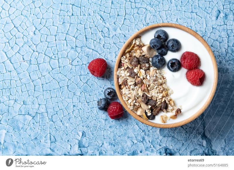 Joghurt mit Beeren und Müsli zum Frühstück in Schale auf blauem Hintergrund Blaubeeren Schalen & Schüsseln Zerealien Nahaufnahme Molkerei lecker Dessert Diät