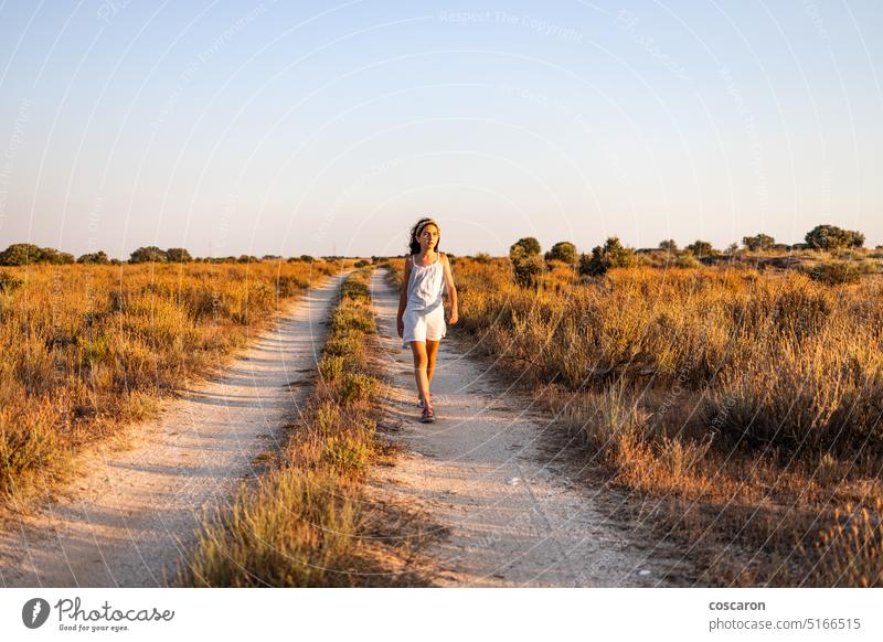 Einsames Mädchen, das bei Sonnenuntergang auf einer Landstraße spazieren geht. schön Schönheit Blauer Himmel Kaukasier Kind Kindheit Kinder Landschaft Tag